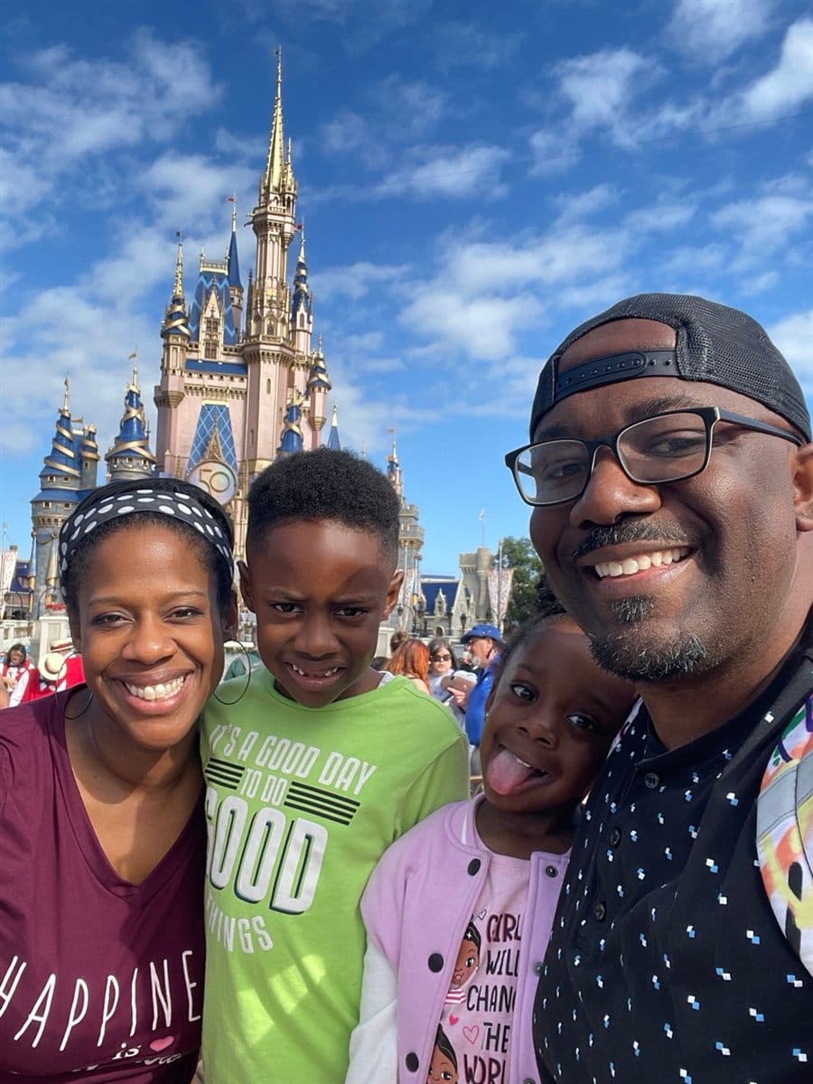 Garaudy Joseph with his wife and two children in front of a theme park castle